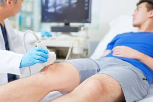 Patient undergoing ultrasound scan performed by doctor before knee surgery in exam room